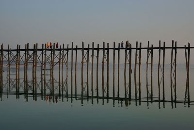 People walking on footbridge with reflection in sea against sky