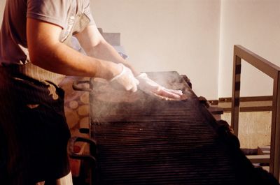 Midsection of man preparing meat on barbecue grill in kitchen