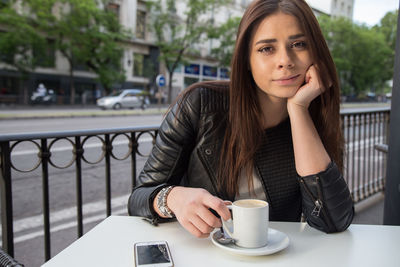 Portrait of young woman having coffee while sitting at sidewalk cafe