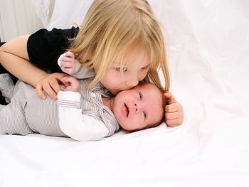 Sister kissing cute brother on bed at home