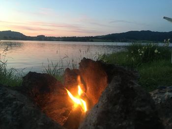 Bonfire by lake against sky during sunset