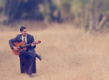 Tilt-shift image of businessman playing guitar on field