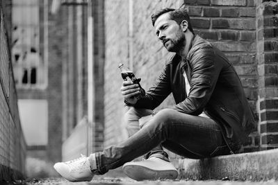 Young man looking away while sitting on wall