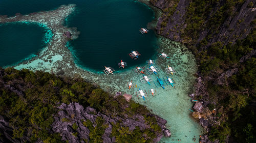 In the photo, a vibrant tropical boat near a beautiful beach or rocky shore.