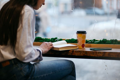 Brunette girl by the window in a cafe drinking coffee, reading a book