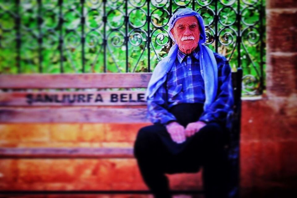 PORTRAIT OF MAN SITTING ON BENCH AGAINST WALL