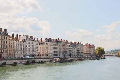 Buildings by river against sky in city