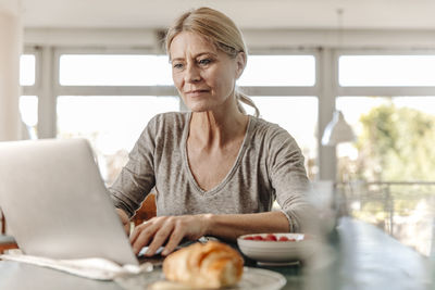 Woman at home having breakfast and using laptop