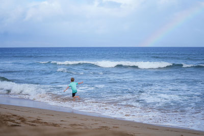 Young boy playing in the waves with a rainbow over the ocean on ka'anapali beach in hawaii. 