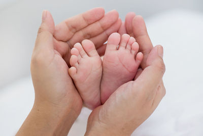 Cropped hands of parent holding baby legs at home