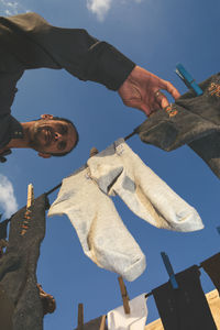 Low angle view of man standing by clothesline against sky