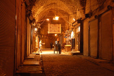 Rear view of man walking on illuminated street amidst buildings at night