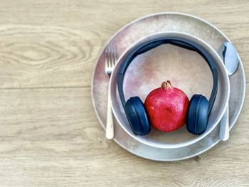 Conceptual shot of pomegranate and headphones in bowl on plate on table with cutlery.