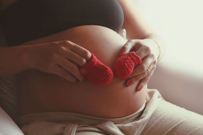 Midsection of pregnant woman holing knitted baby booties on abdomen