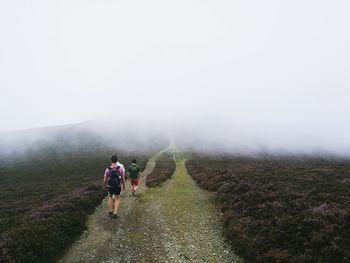 Rear view of men walking on dirt road amidst field