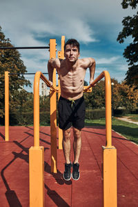 Young shirtless bodybuilder doing dips on parallel bars during his workout in a modern calisthenics