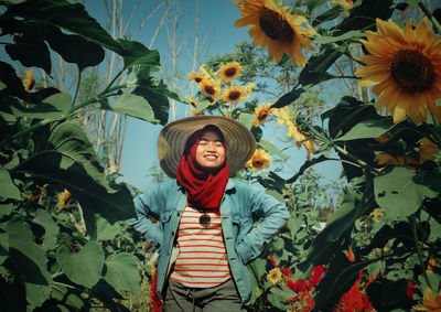 Smiling young woman standing amidst plants against sky