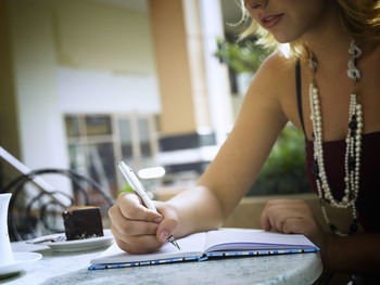 Young woman writing in diary while sitting at table