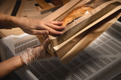 Close-up of female hands packing fresh artisanal bread in a paper bag