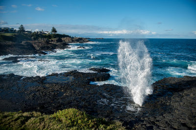 Waves splashing on rocks at shore against sky