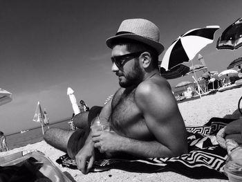 Midsection of shirtless man sitting on beach against sky