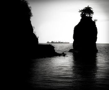 Silhouette tree by sea against clear sky