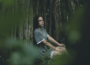 Portrait of woman sitting by tree in forest