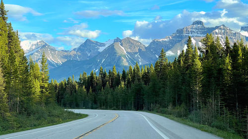 Road amidst trees and mountains against sky