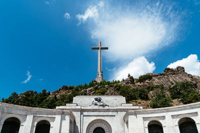 Low angle view of historical building and cross against blue sky