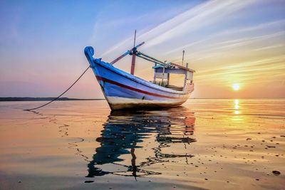 Fishing boat moored on beach against sky during sunset