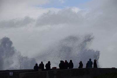 Silhouette people by splashing water against sky