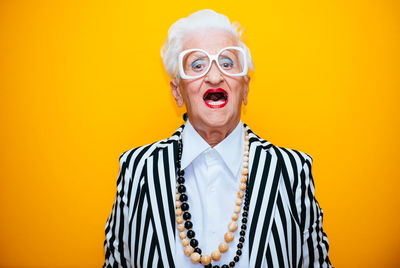 Portrait of stylish senior woman standing against yellow background