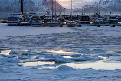 Scenic view of frozen lake with boats against mountain