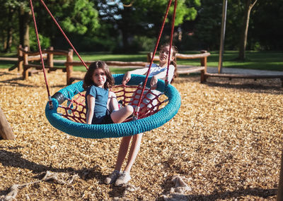 Portrait of girls the older one swings the younger one on a round rope swing