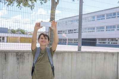 Teenage boy taking selfie while standing against school