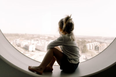 Full length of girl sitting on window sill in hotel room