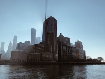 Modern buildings by river against clear blue sky in city