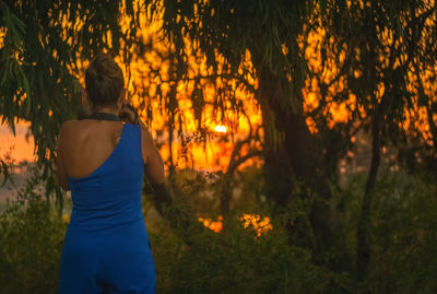 Rear view of beautiful woman photographing trees during sunset