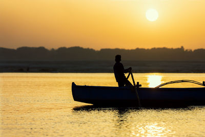 Silhouette man in boat against sky during sunset