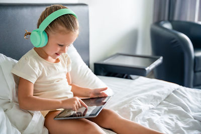 Boy using digital tablet while sitting on bed at home