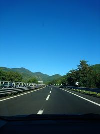 Road amidst trees against clear blue sky seen through car windshield