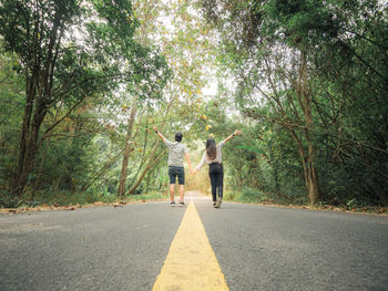 Rear view of couple holding hands while walking on road amidst trees