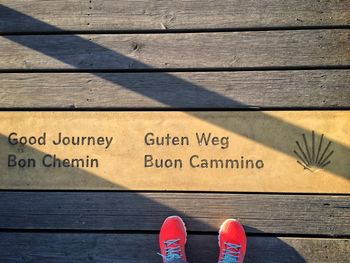 Low section of person wearing red shoes standing by text on wooden floorboard