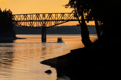 Yacht below agate pass bridge against sky during sunset