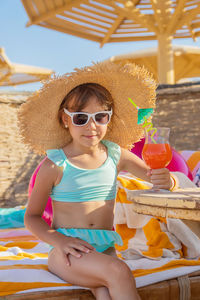 Portrait of young woman wearing sunglasses while sitting at beach