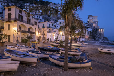 Sailboats moored on street by buildings in city at dusk