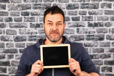 Portrait of man holding writing slate against wall