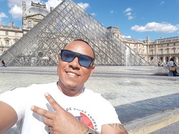 Portrait of happy man wearing sunglasses while standing against louvre museum