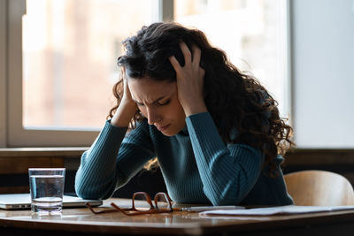 Unhappy woman overworked stressed sit at desk with closed laptop suffer from headache or depression