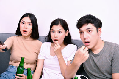 Shocked young friends watching soccer match on sofa at home